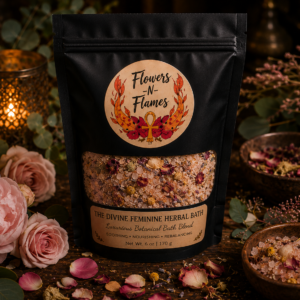 Flowers N Flames Divine Feminine Herbal Bath in a matte black stand-up pouch with a kraft label, surrounded by pink flowers, rose petals, botanical herbs, and warm candlelight on a rustic wooden surface.