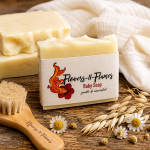 Handcrafted Flowers N Flames Baby Soap resting on a rustic wooden surface beside a soft white towel, oats, chamomile flowers, and natural botanicals, wrapped in the signature kraft label.