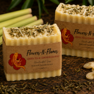 Handcrafted Flowers N Flames Green Tea Lemongrass Soap displayed on a rustic wooden surface with fresh lemongrass stalks, green tea leaves, sliced lemons, and botanical accents wrapped in the signature kraft paper label.